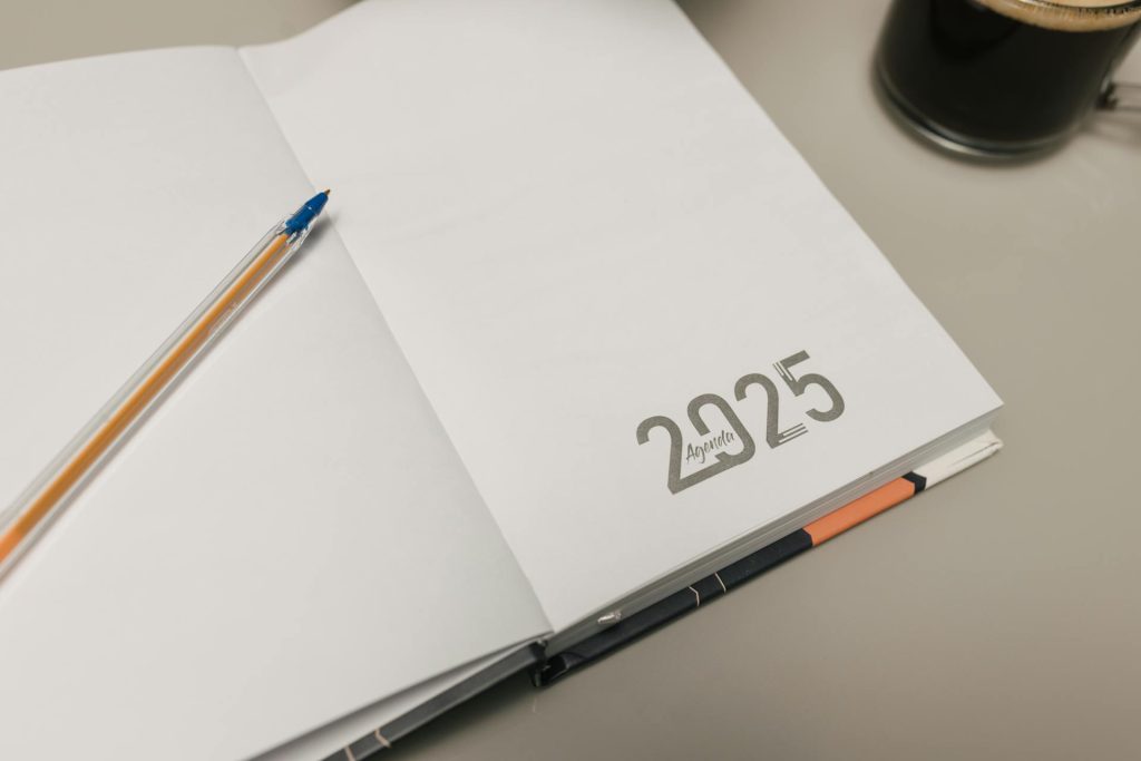 Open planner with pen and coffee on desk. The year, 2025, is written on the planner